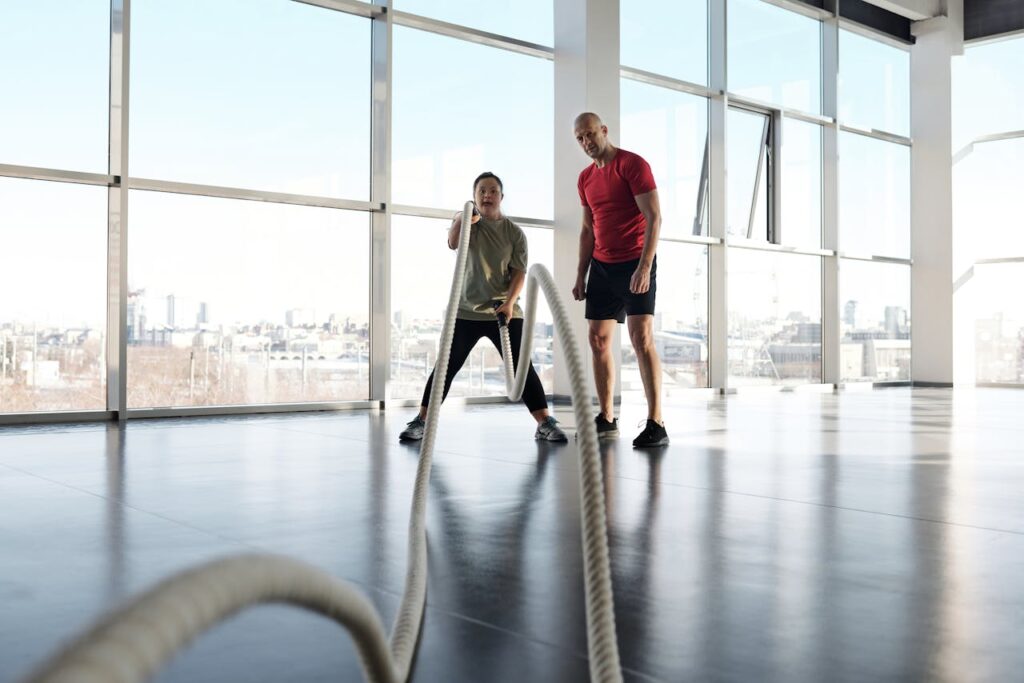 Man with Down Syndrome working out with ropes in a modern gym with a trainer.