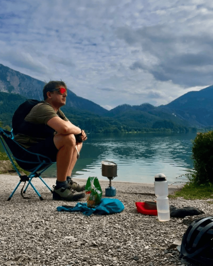 Pause beim Bikepacking an einem Bergsee in den Alpen mit Campingkocher und Ausrüstung